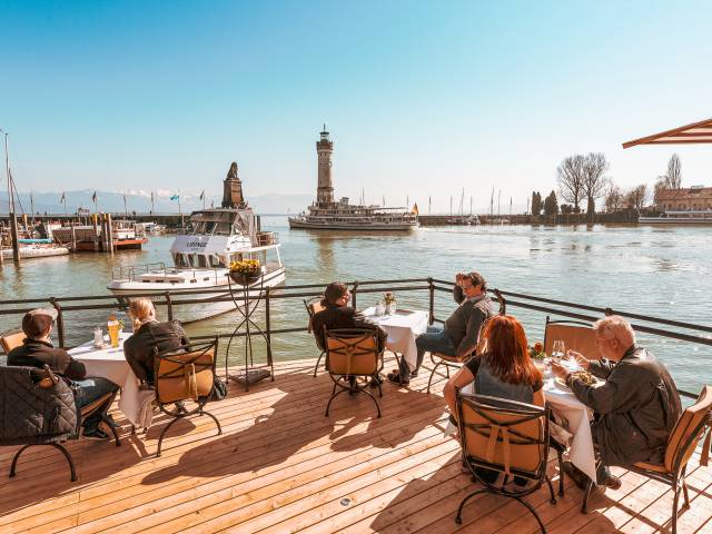 Personen sitzen auf der Habour Lounge mit Blick auf den Hafen der Insel Lindau