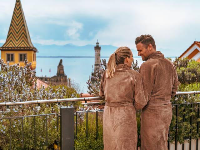 Paar im Bademantel genießt die Aussicht vom Spabereich auf den Bodensee