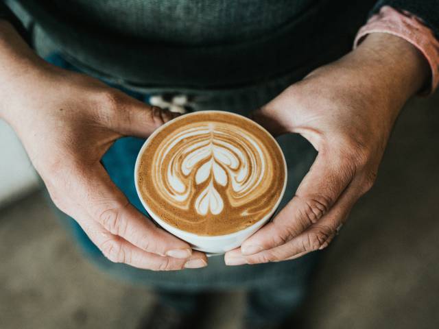 Person hält eine Kaffeetasse mit einem Schaummuster in der Hand