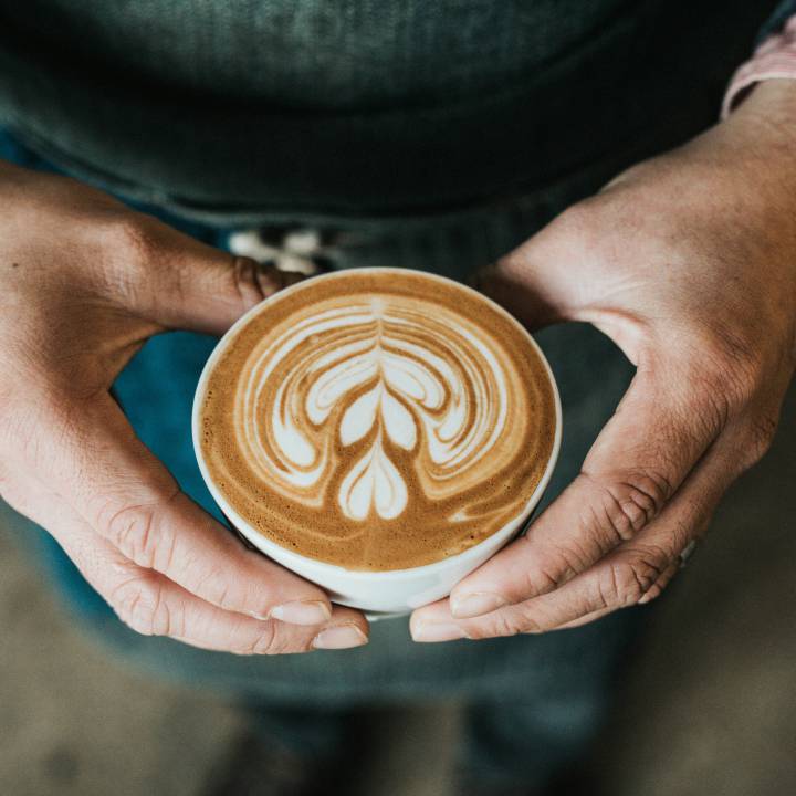 Person hält eine Kaffeetasse mit einem Schaummuster in der Hand